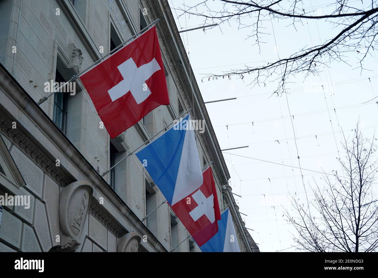 Detail of a Swiss federal flag and flag of canton Zurich displayed on the facade of a historic building in the city center of Zurich. Low angle view. Stock Photo