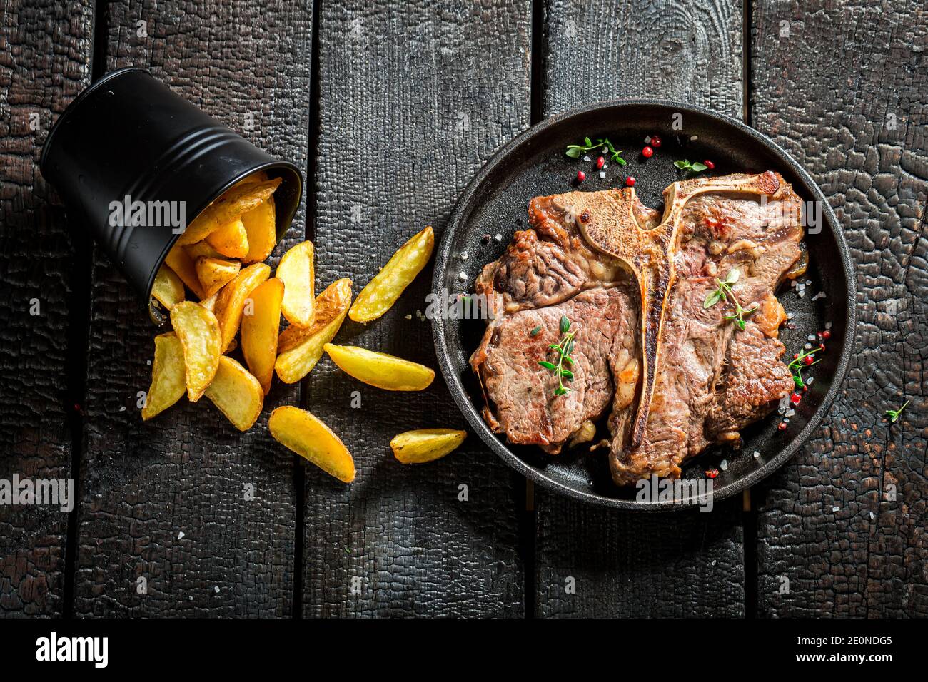 Closeup of hot well done tbone steak and chips with herbs on the burnt table Stock Photo Alamy