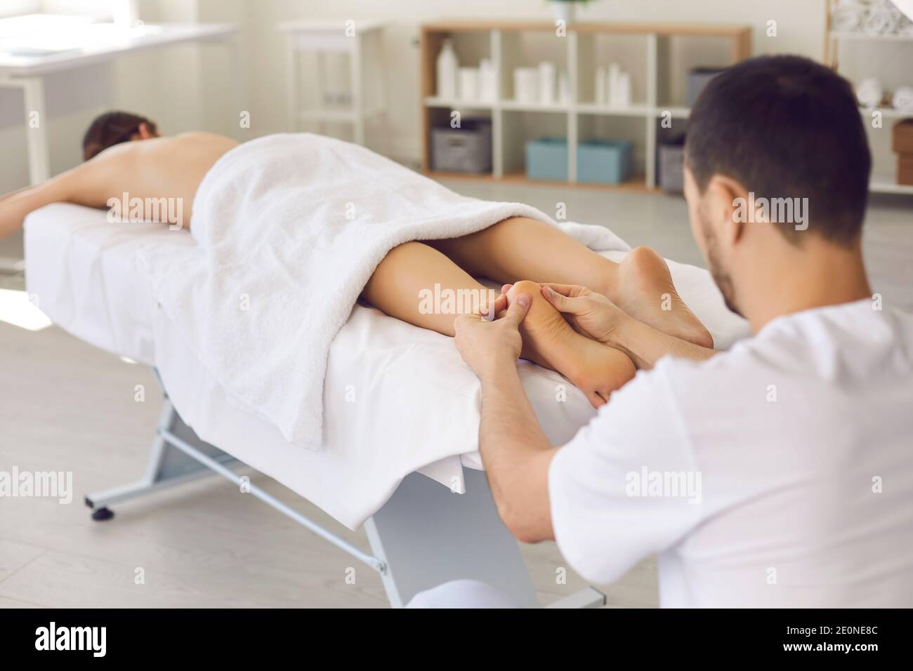 Man masseur chiropractor in white uniform massaging lying relaxing womans heels Stock Photo