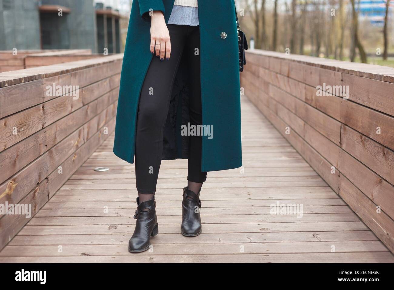 Black ankle boots, black leather bag, warm emerald coat and black trousers. Stylish and fashionable girl on a walk. Stock Photo