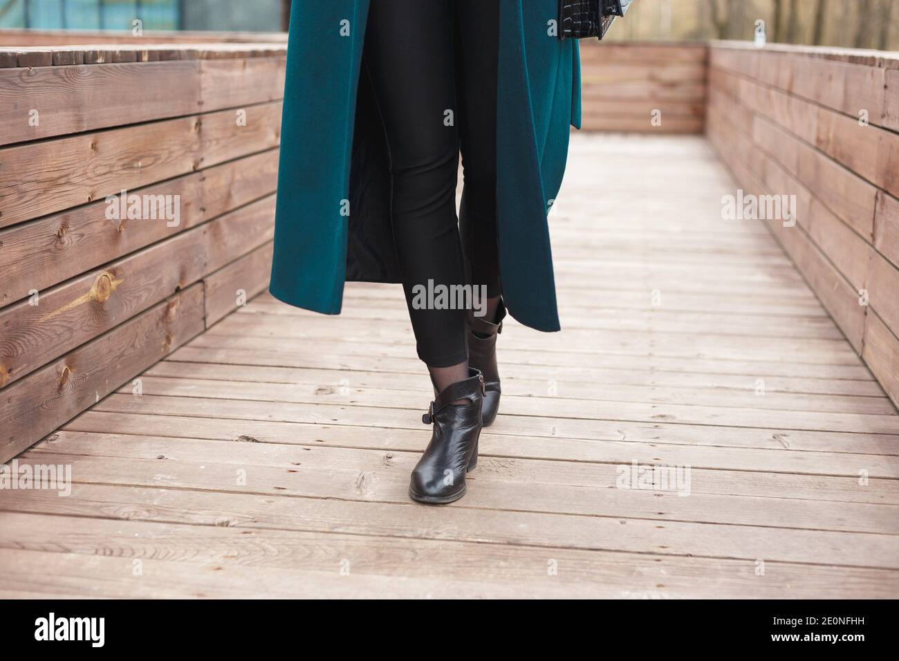 Black ankle boots, black leather bag, warm emerald coat and black trousers. Stylish and fashionable girl on a walk. Stock Photo