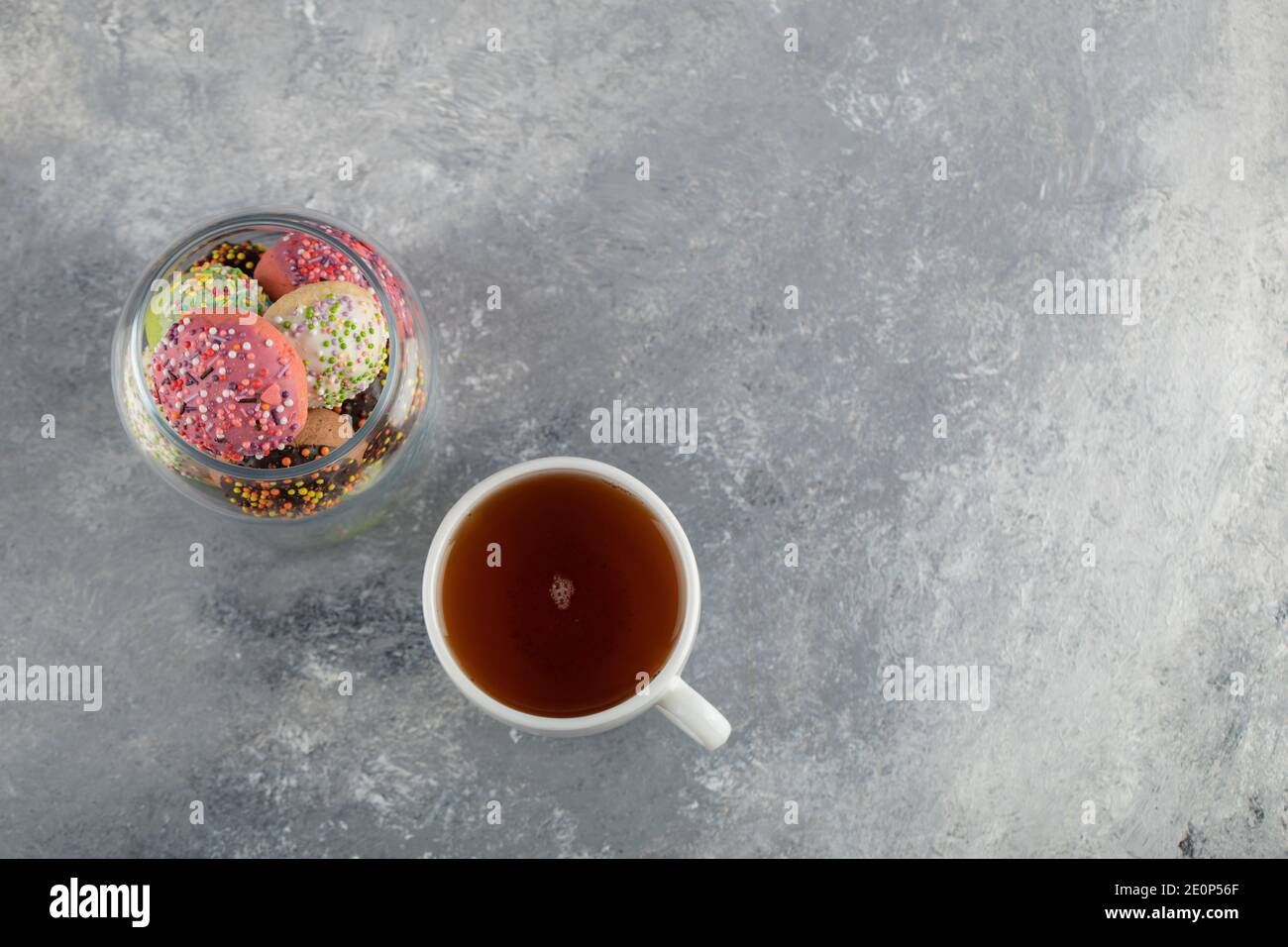 A glass jar full of small colorful doughnuts with a cup of hot tea Stock Photo