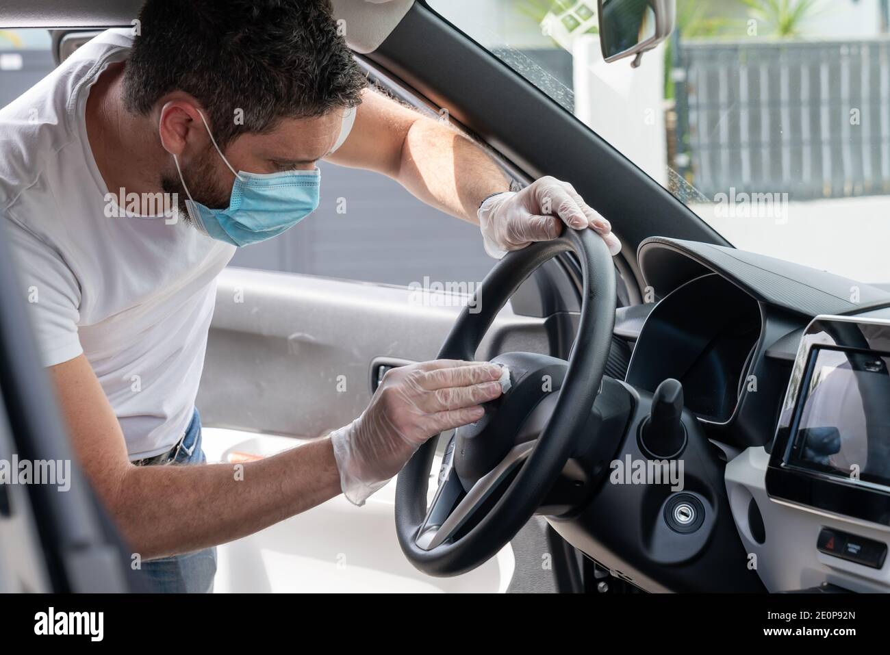 Covid-19, man with medical mask and gloves disinfects his car with a cleaning cloth Stock Photo
