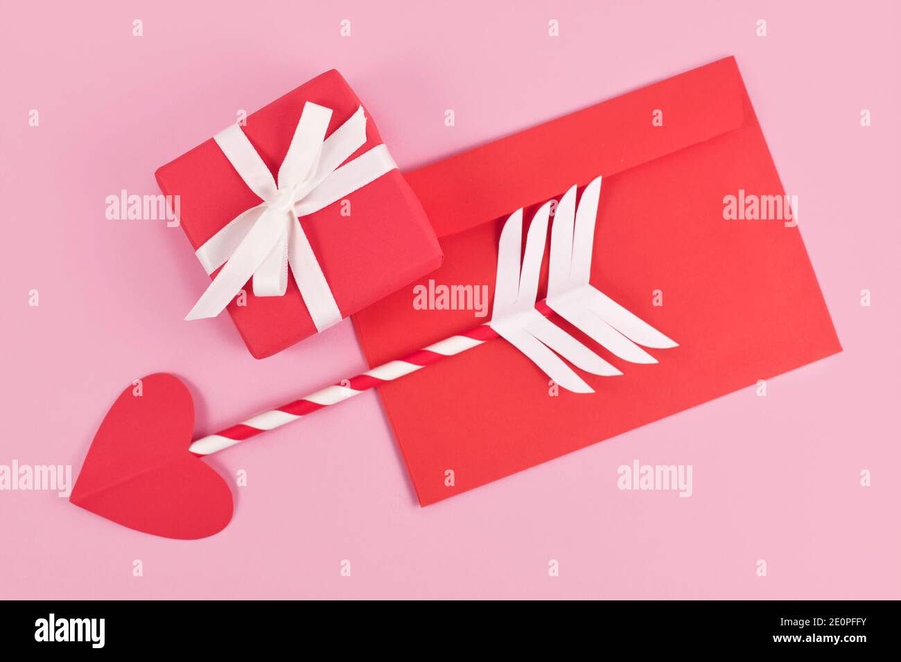 Cute paper cupid love arrow with heart shaped tip, love letter and gift box for Valentine's Day on pink background Stock Photo