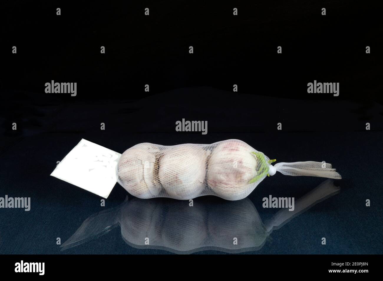 The Garlic in net rests upon glass table with reflection. Products of the feeding on black background Stock Photo