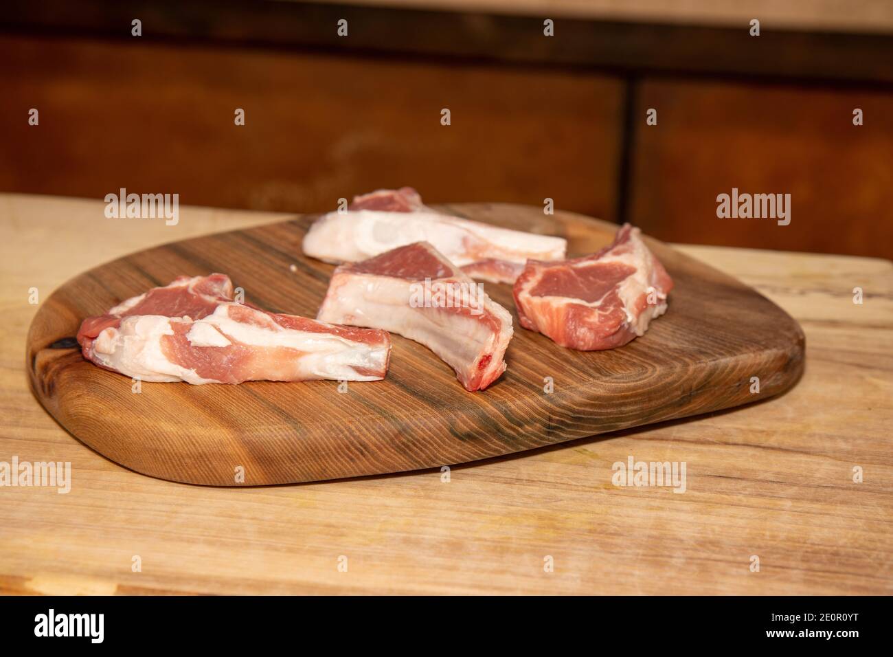 Four raw lamb chops on a wooden kitchen work top Stock Photo