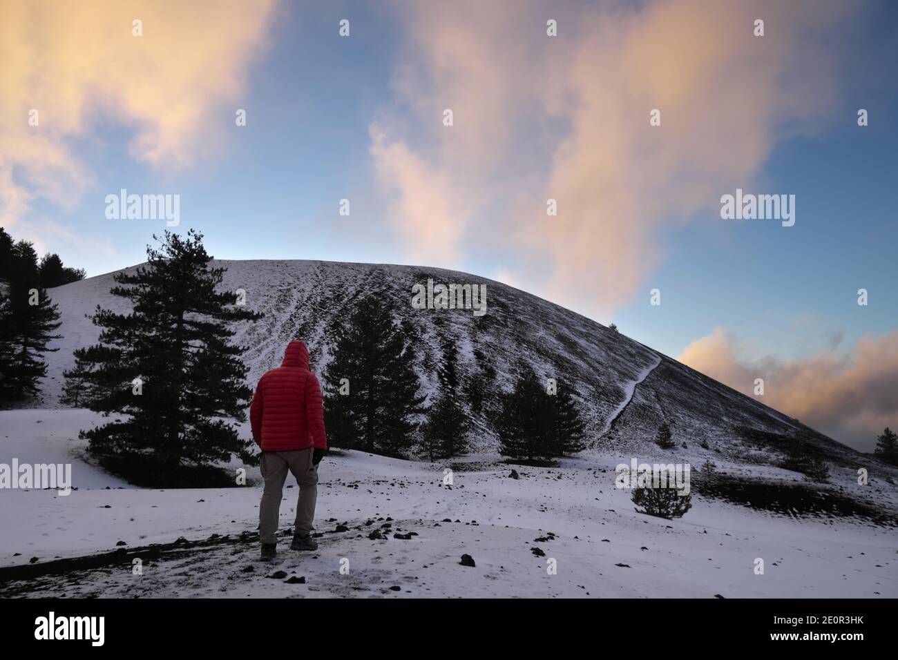 man walking on the snow at the sunset towards a volcanic cone of Etna Park a landmark in Sicily of hiking in winter Stock Photo