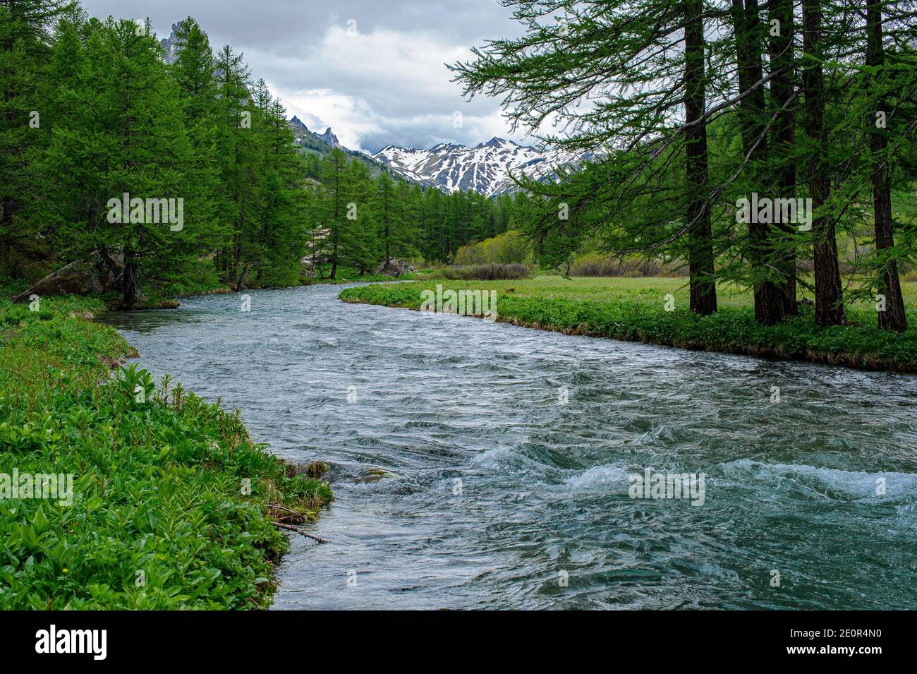 View of the Claree River in the Hautes-Alpes. The banks are covered with grass and, in the background, some mountains still bearing snow patches. Stock Photo