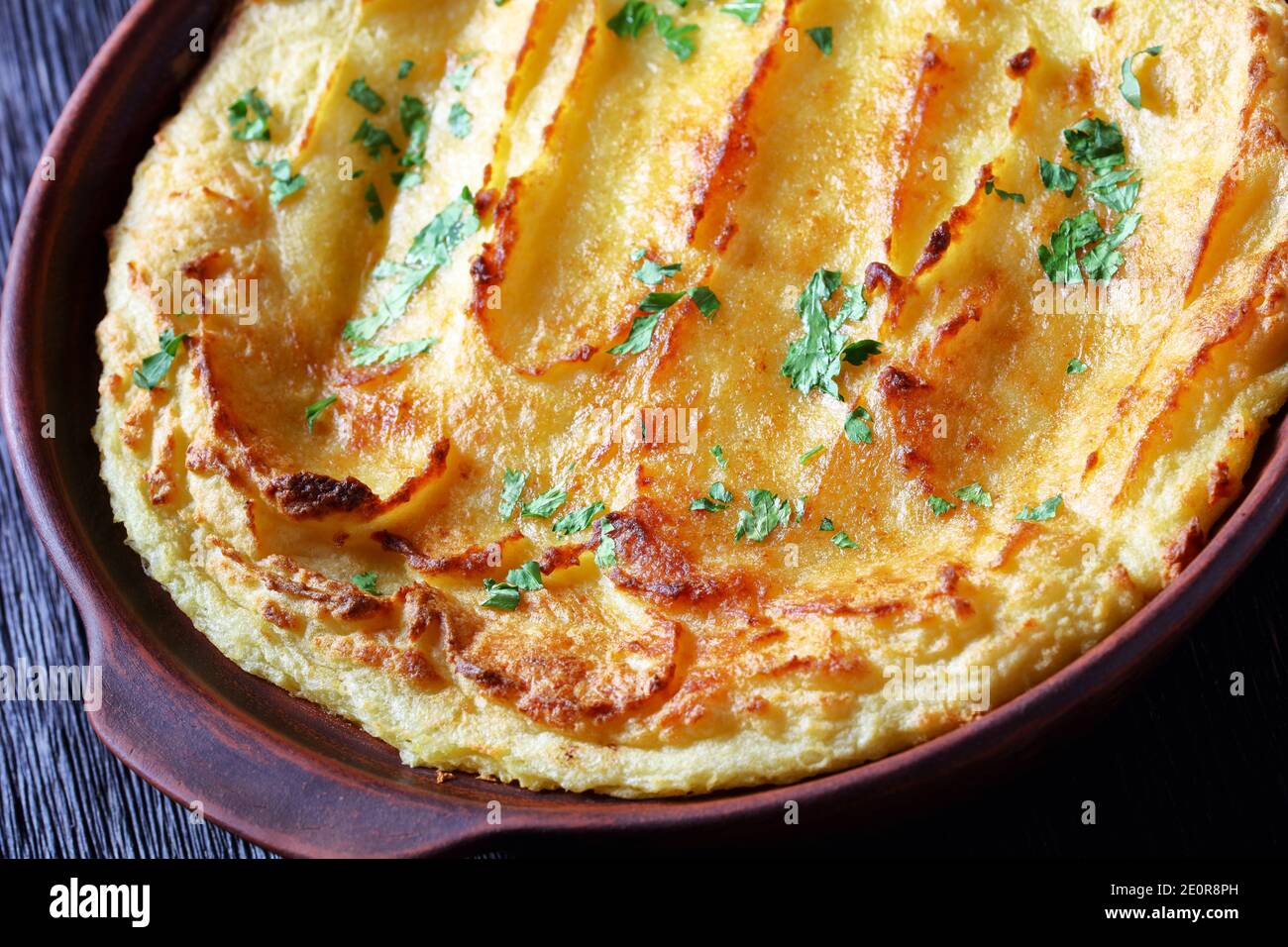 Garlic Parmesan Mashed Potato Casserole sprinkled with parsley in a dish on dark wooden table, horizontal view from above, close-up Stock Photo