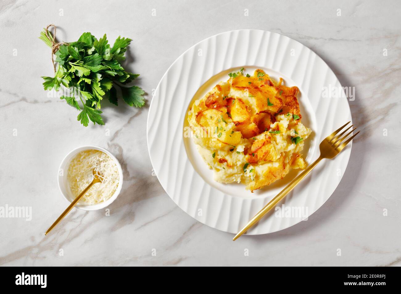 portion of baked Mashed Potato Casserole sprinkled with parsley on a white plate with golden fork, on a marble table, horizontal view from above, flat Stock Photo