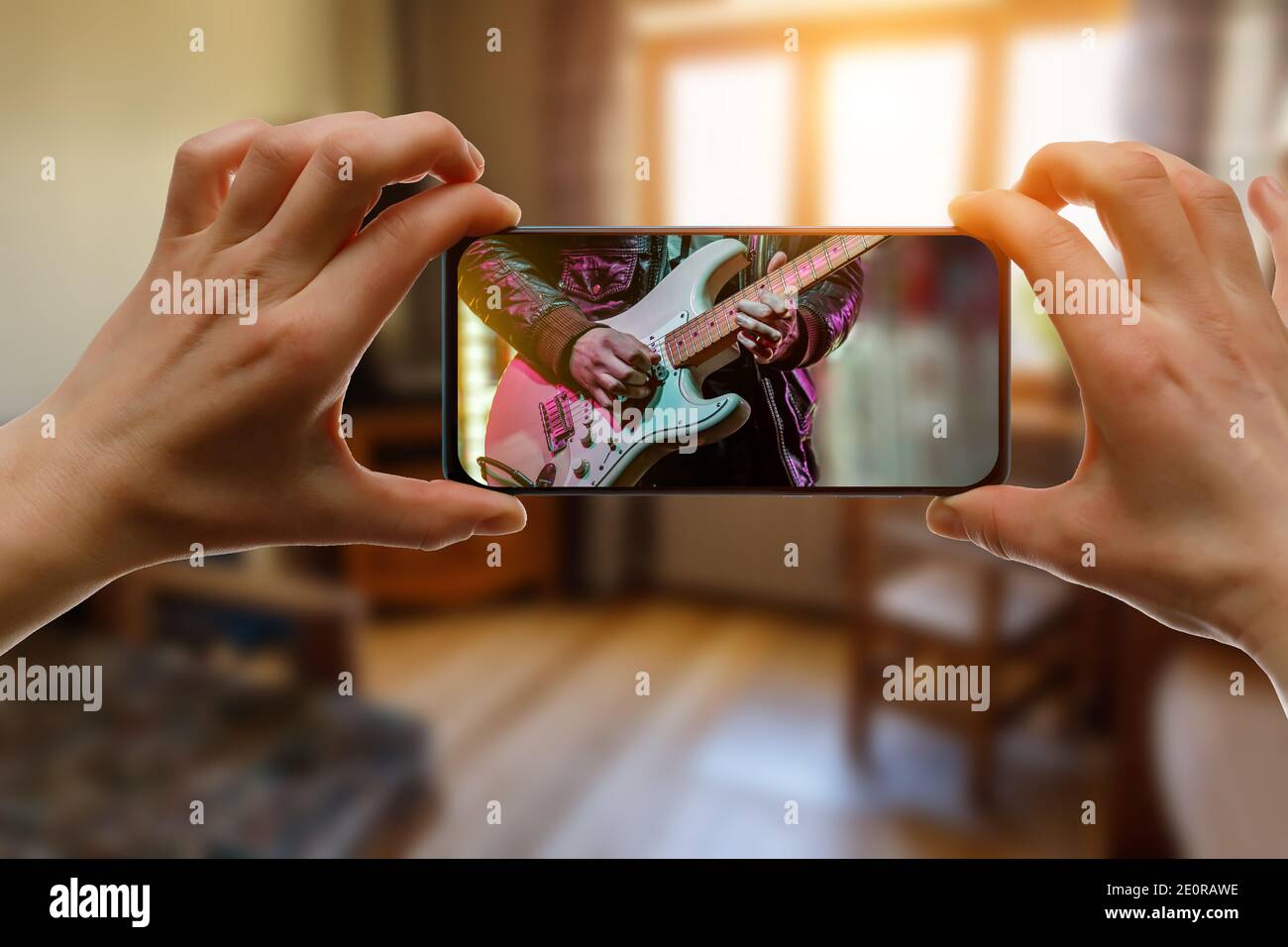 Online music lesson via mobile phone at home. Guitar teacher hands on screen. Stock Photo