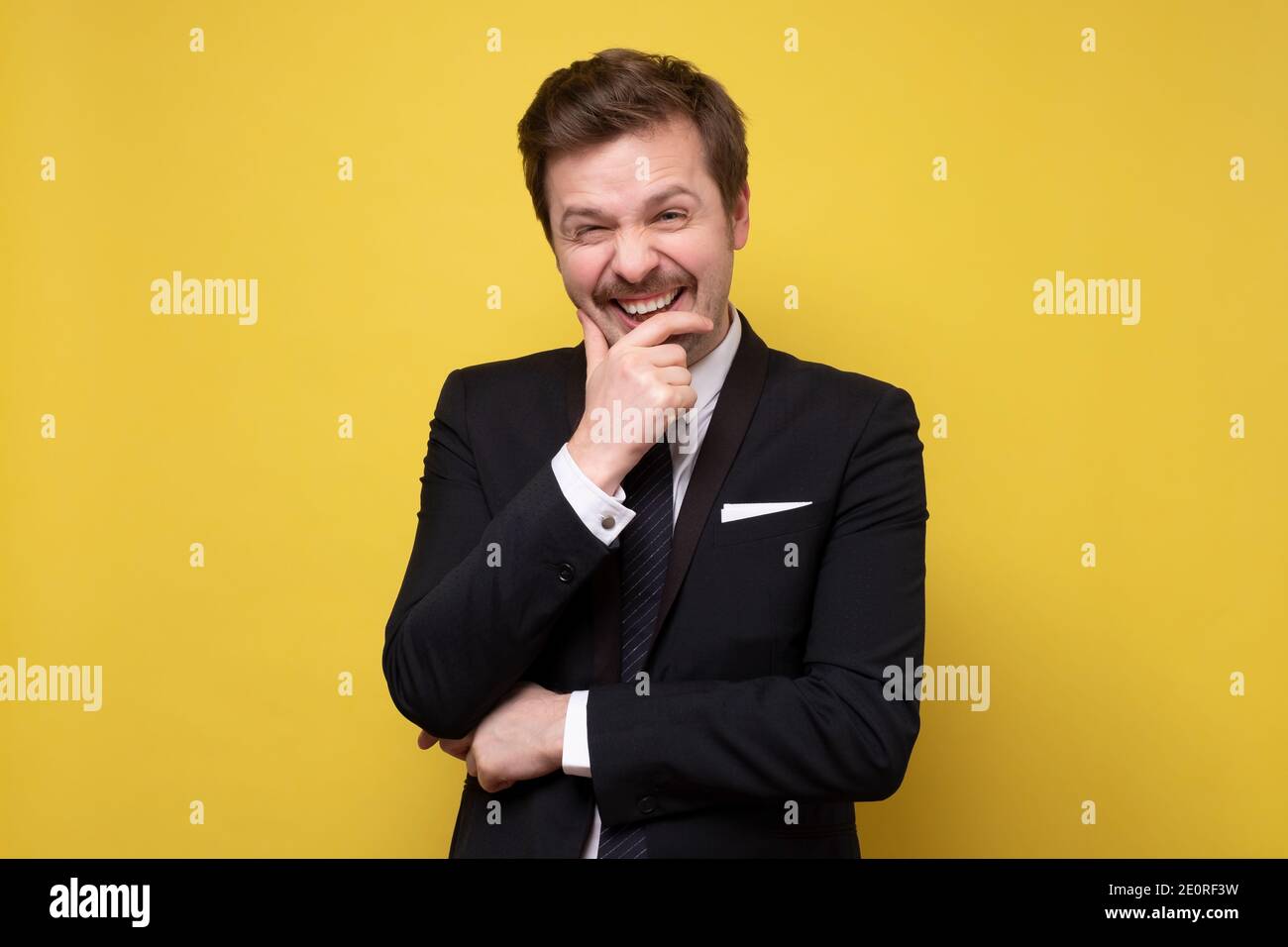 Young happy cheerful young man in suit laughing on your joke. Studio shot on yellow wall. Stock Photo