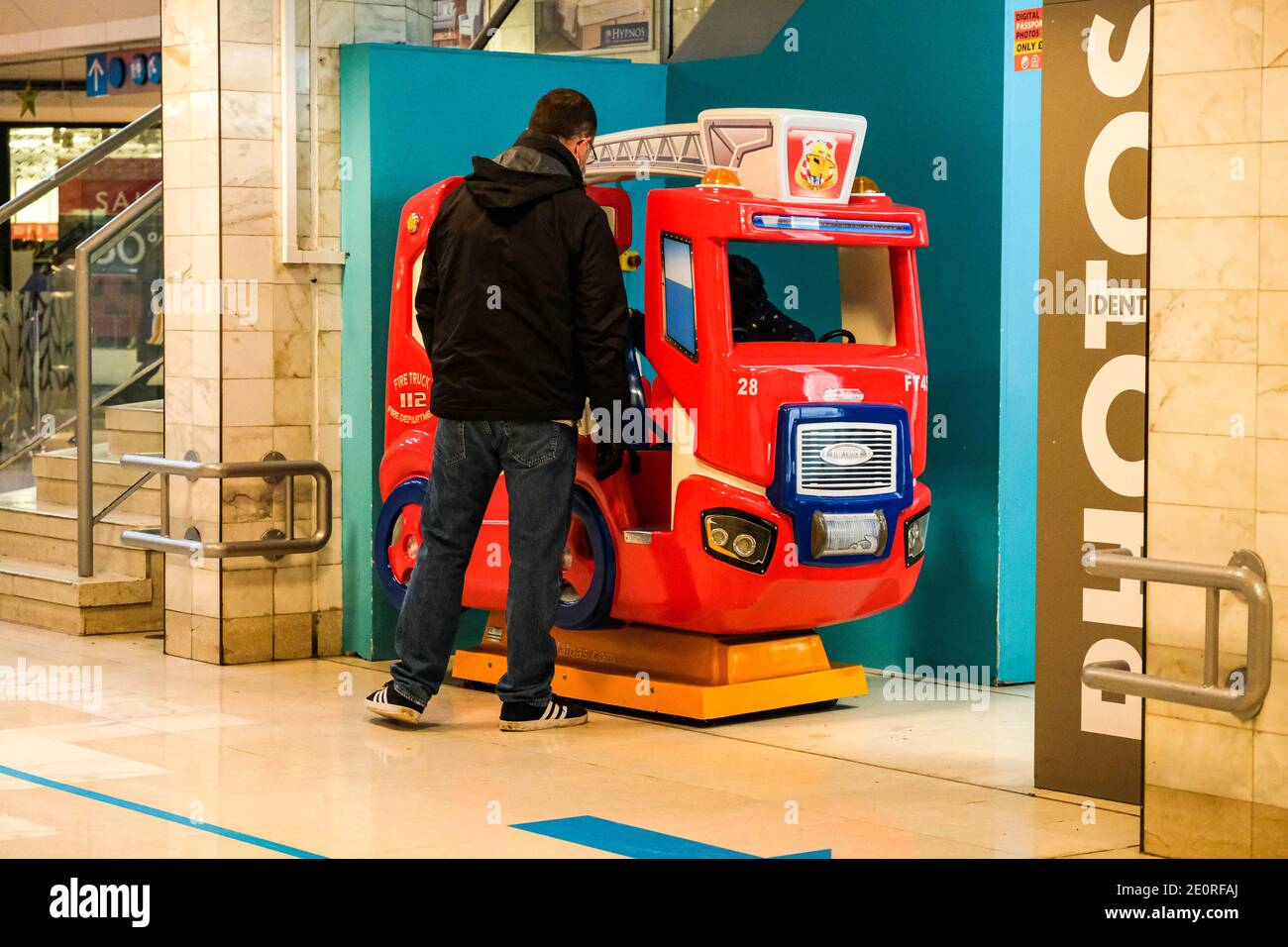 London UK, January 02 2021, Father Or Man Supervising His Child On A Toy Fire Engine Fairground Style Ride Stock Photo