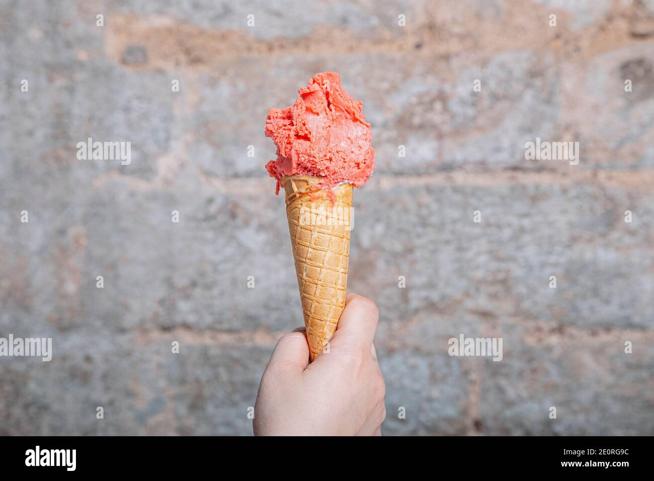 Hand holding strawberry flavor artisan ice cream cone. Strawberry ice cream served in a waffle