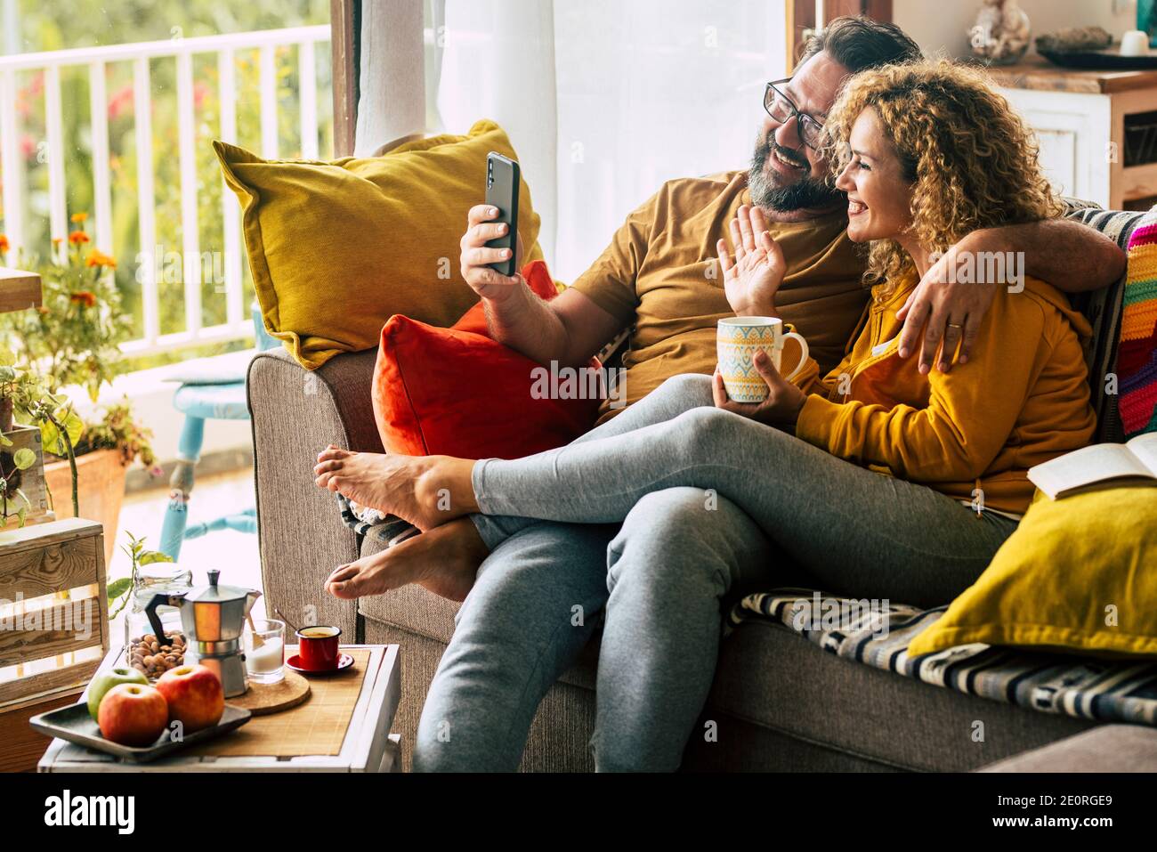 Adult happy couple man and woman at home enjoy morning breakfast and do video phone call to friends or parents - cheerful caucasian people indoor acti Stock Photo