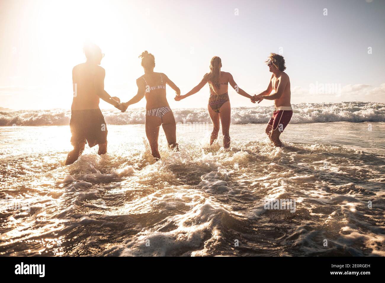 Group of friends enjoy summer holiday vacation at the beach running together in the sea water during a golden sunset - people and travel activity in t Stock Photo