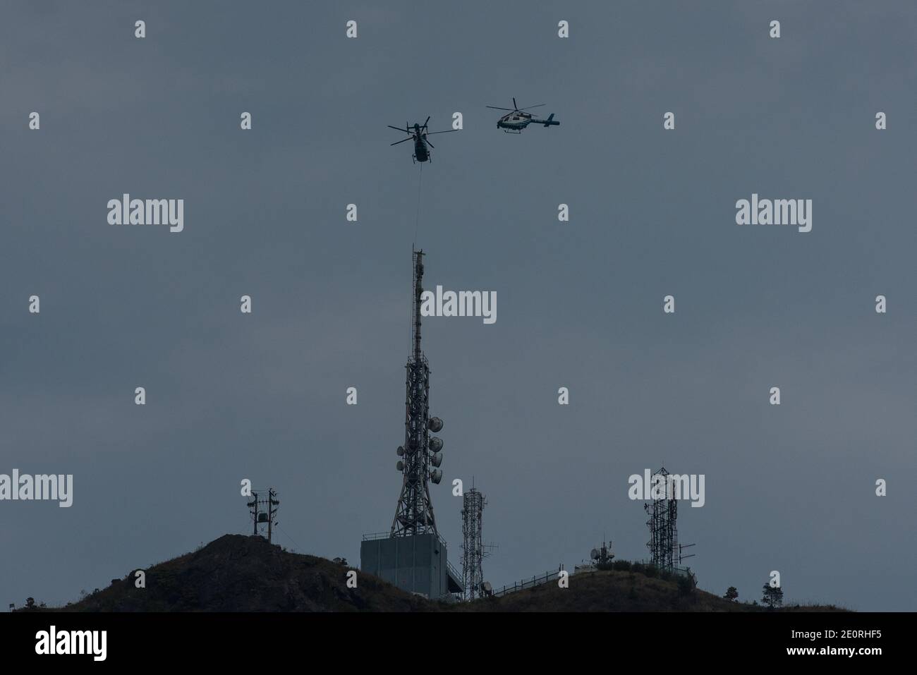 Two helicopters fly above the radio antenna of Kowloon Peak. Stock Photo