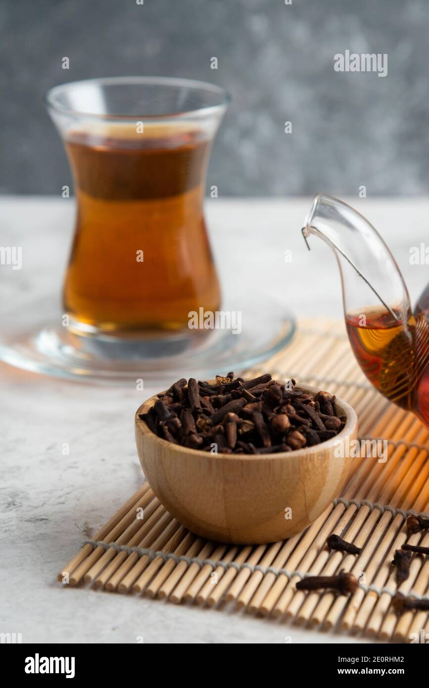 A glass cup of tea with dried cloves and teapot Stock Photo