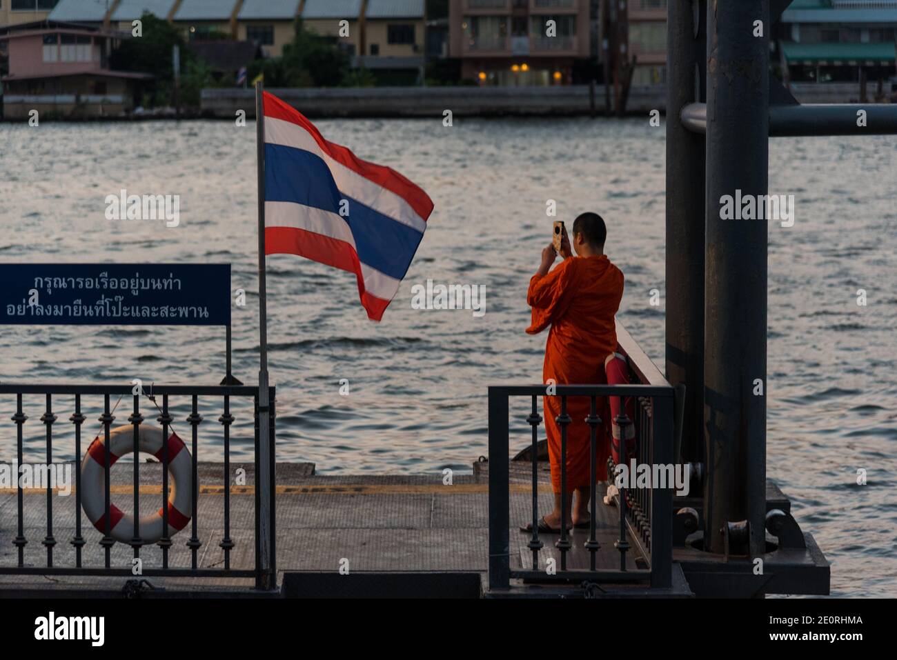 A Buddhist monk takes a picture of sunset with his smartphone on the banks of the Chao Phraya river in Bangkok, Thailand. Stock Photo