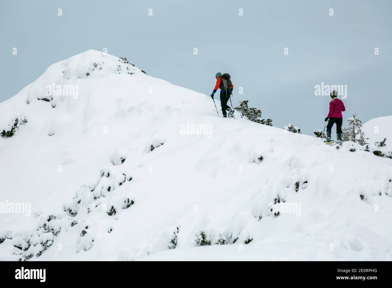 Two hikers alpinists climbing up the snowy mountain on Sunset. Alpine winter view. Carpathians, Marmarosy Stock Photo