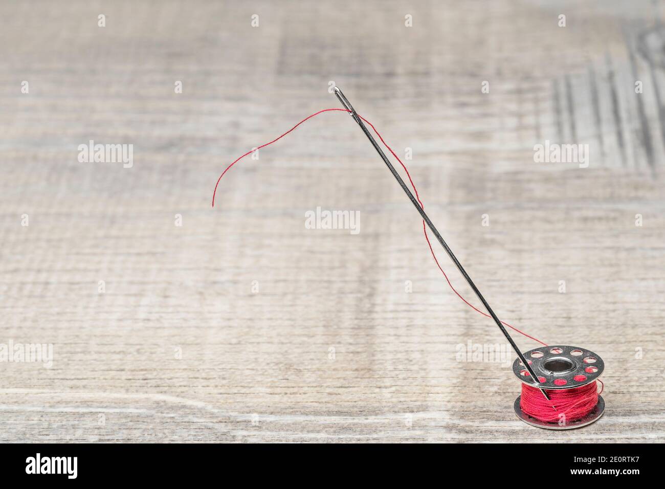 Bobbin and needle with red thread on a wooden background Stock Photo