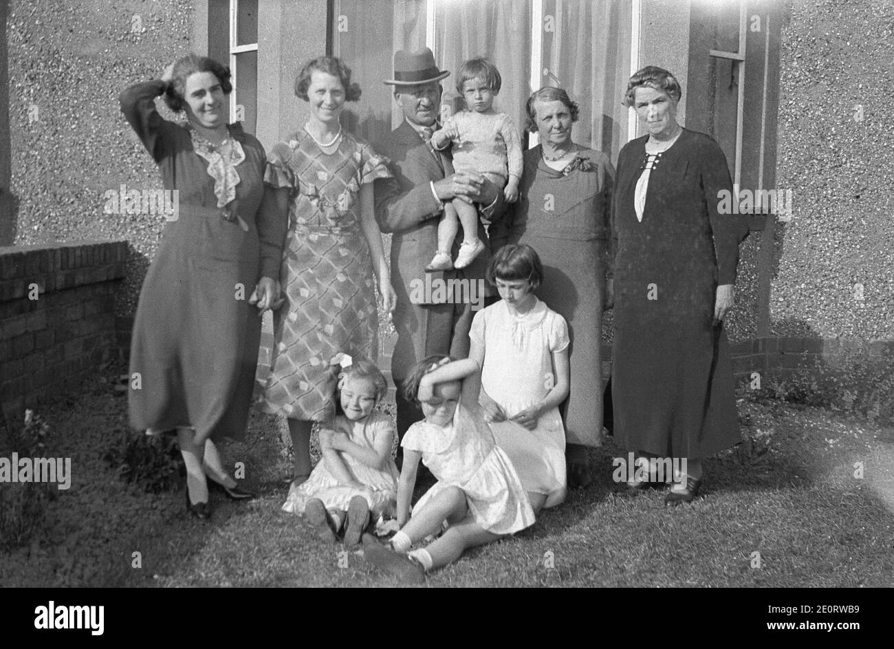 In a front garden outside a pebble dash semi-detached house, a family picture, circa 1930s, of a mother, sisters, grandparents and children, showing the male and female fashions of the day, England, UK. Stock Photo