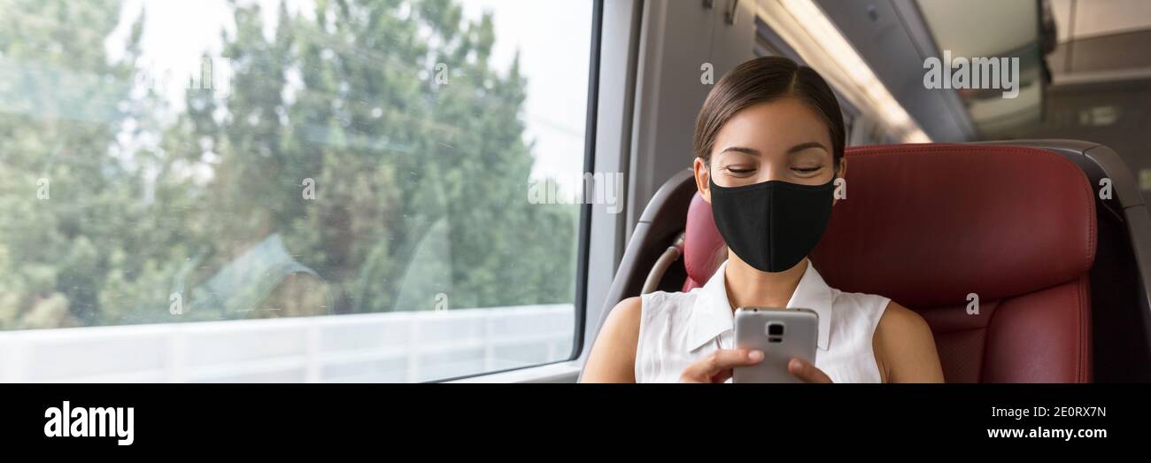 Train passenger Asian business woman using mobile phone during travel commute wearing face mask for corona virus pandemic. Panoramic banner of Stock Photo