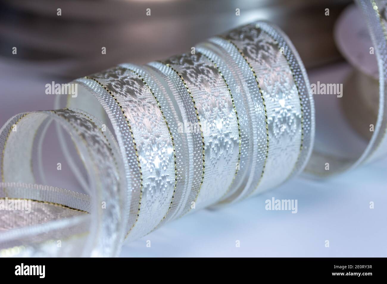 Macro defocused full frame texture abstract of shimmering silvery white brocade fabric ribbon, with golden accent stitches on a white background Stock Photo