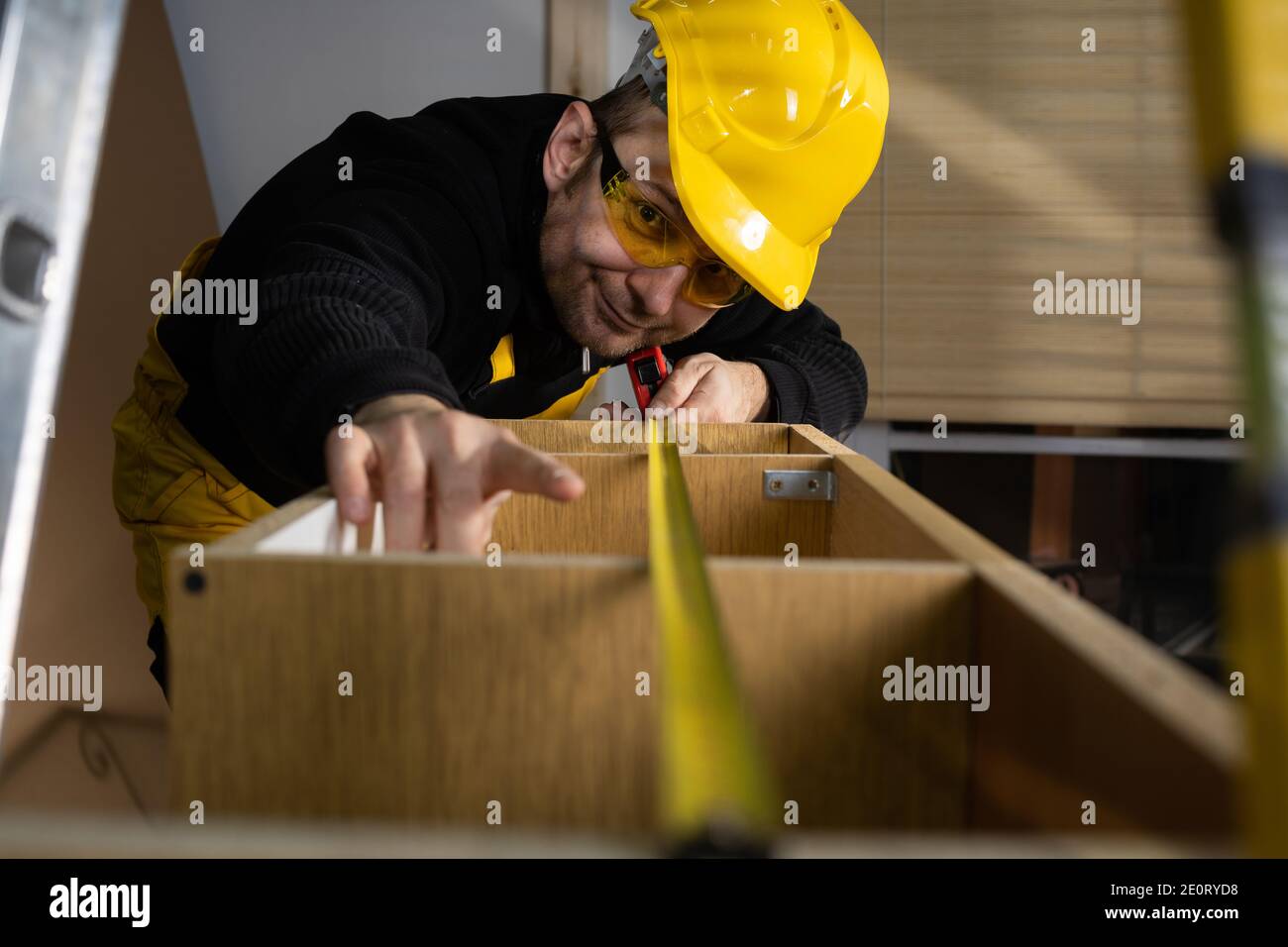The construction worker measures the top of the cabinet to check if it is made correctly with the designed dimensions. Wearing personal protective equipment. Stock Photo