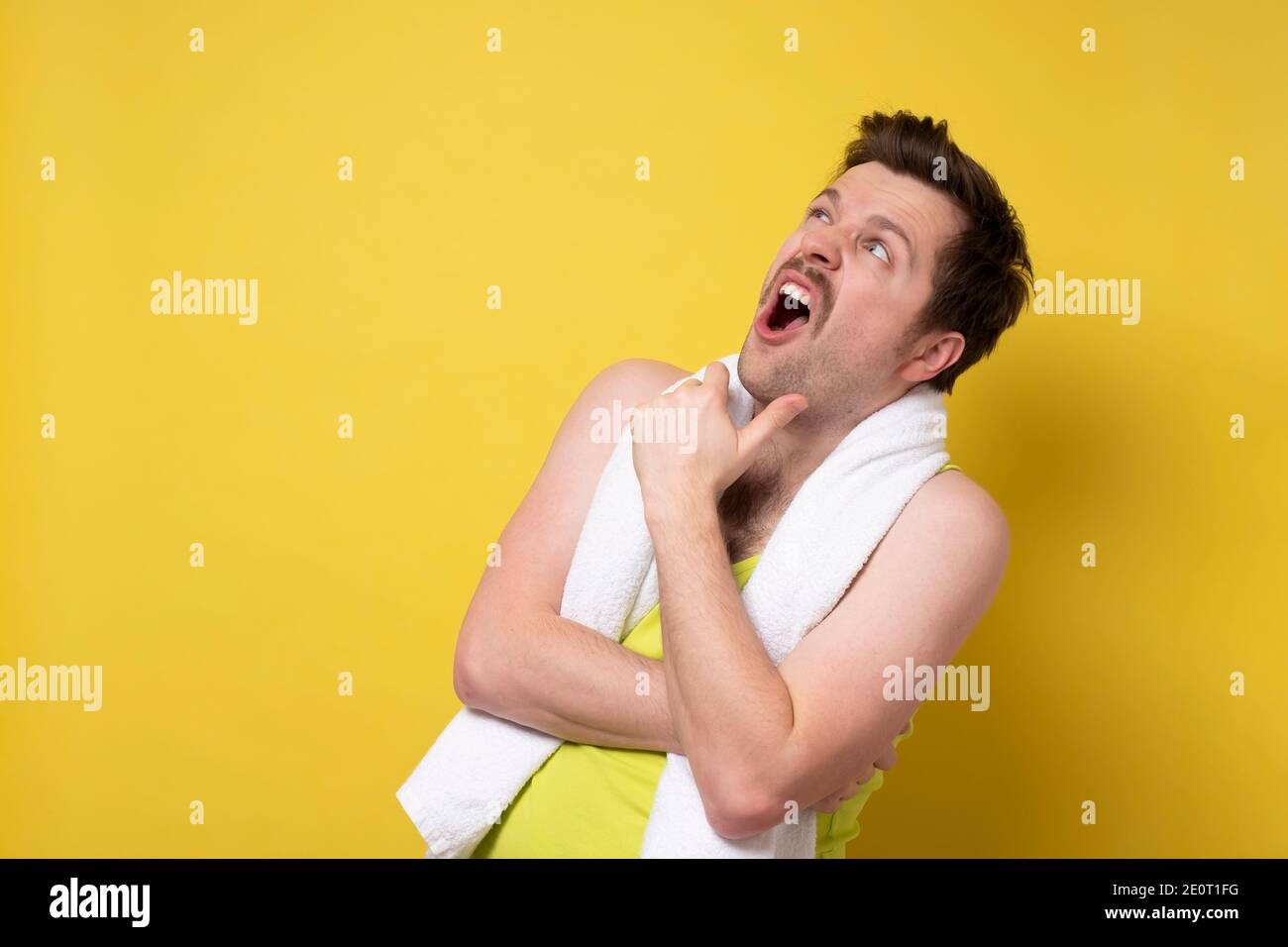 Young caucasian sport man with towel being surprised looking up. Studio shot on yellow wall. Stock Photo