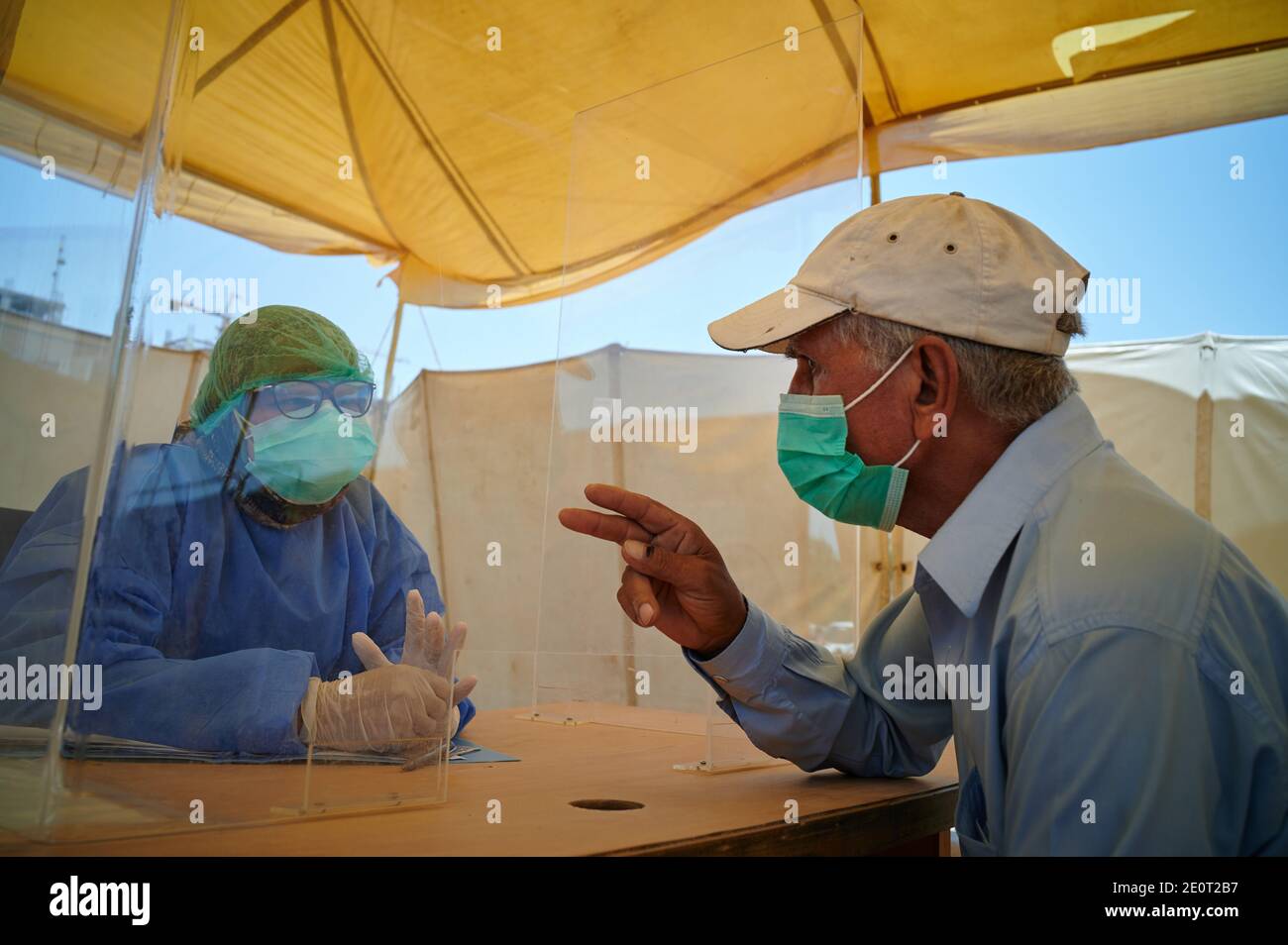 A health worker dressed in full PPE sits behind a flexi glass shield and counsels a TB client for a coronavirus test, at the Gori TB Clinic at the Indus Hospital in Korangi, Karachi, Pakistan. Stock Photo