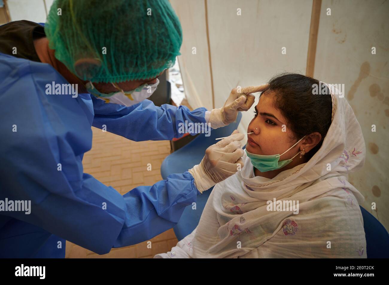 A lab technician dressed in full PPE gear, takes a nasal specimen from Farhad Khalil, 20,  a TB client for a coronavirus test, at the Gori TB Clinic at the Indus Hospital in Korangi, Karachi, Pakistan. Stock Photo