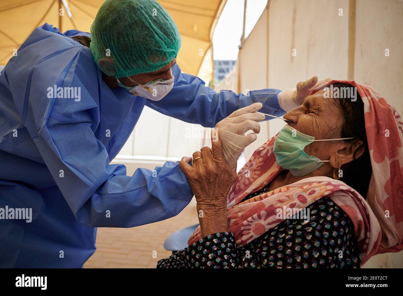 A lab technician dressed in full PPE gear, takes a nasal specimen from Kaneez Fatima, 60, TB client for a coronavirus test, at the Gori TB Clinic at the Indus Hospital in Korangi, Karachi, Pakistan. Stock Photo