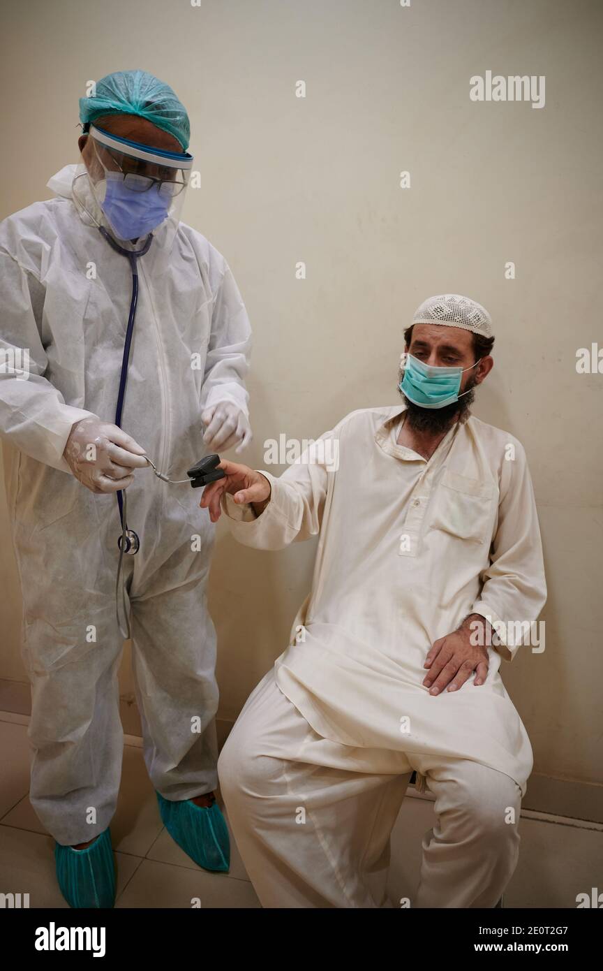 Amidst the coronavirus pandemic that continues to rise in the country rapidly,  Dr. Saeed-ur-Rehman, dressed in full PPE gear uses pulse oximeter to measure oxygen saturation level of a TB patient who recently contracted COVID-19, at a community health centre in Shiri Jinnah neighbourhood in Karachi, the main port city of Pakistan. Stock Photo