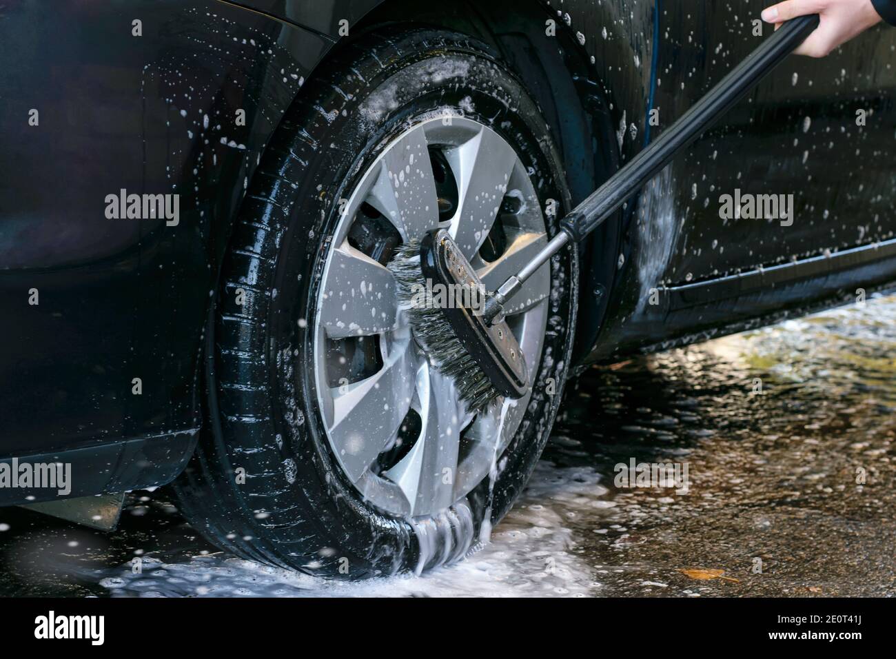 Car wash outdoor. Washing car wheel with a washing brush, close up