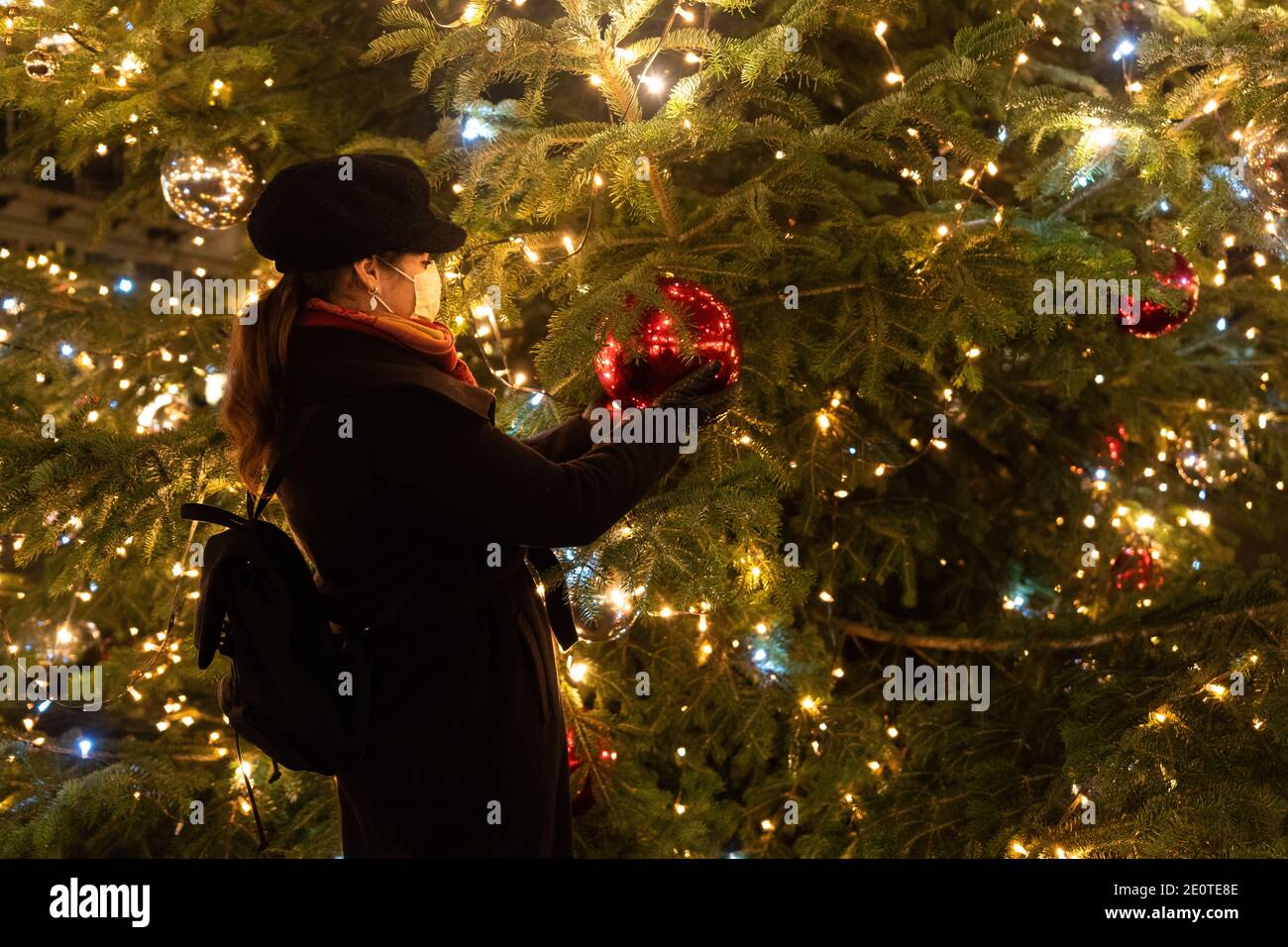 Woman holding Christmas giant red bauble. Woman with mask stands in front of big Christmas tree. Stock Photo