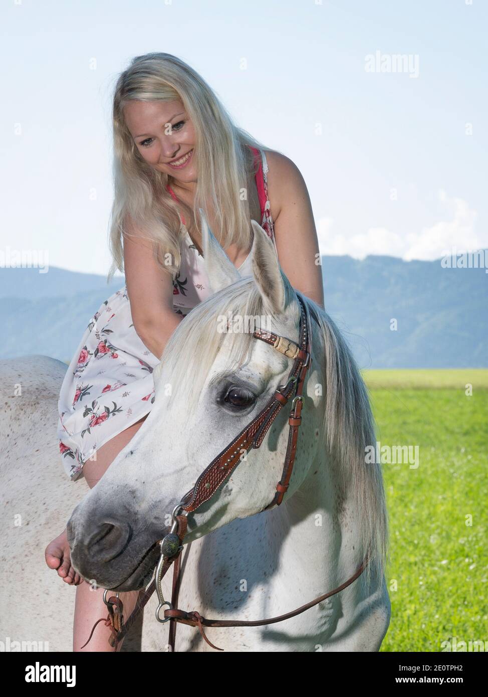 Young Pretty Woman With Long Blond Hair Is Sitting In Summer Dress On Her Horse Stock Photo