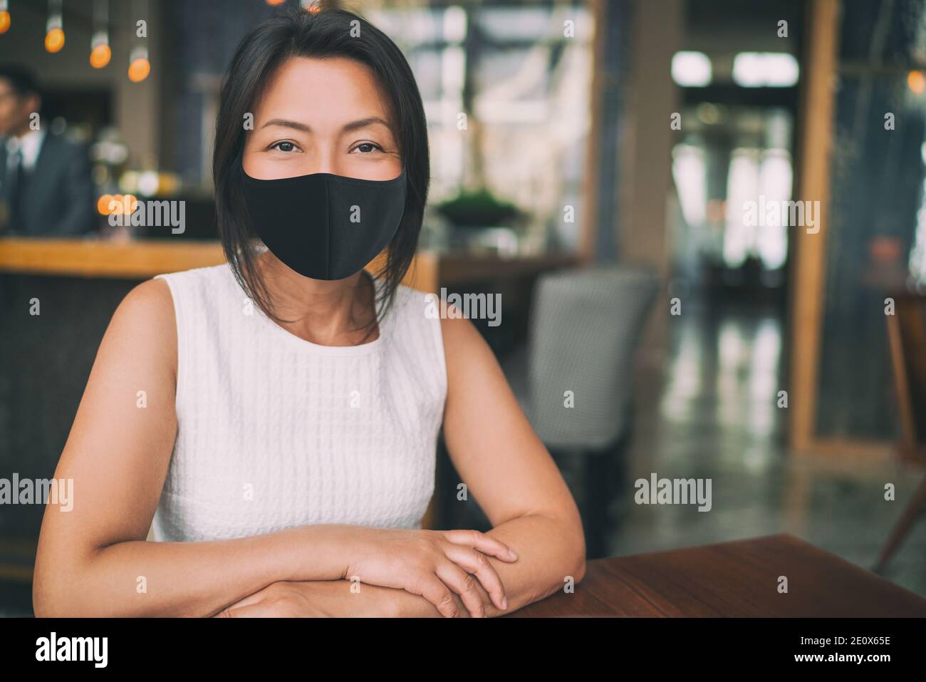 Asian mature business woman wearing protective face mask for coronavirus prevention in indoors public space as work office, restaurant, cafe Stock Photo
