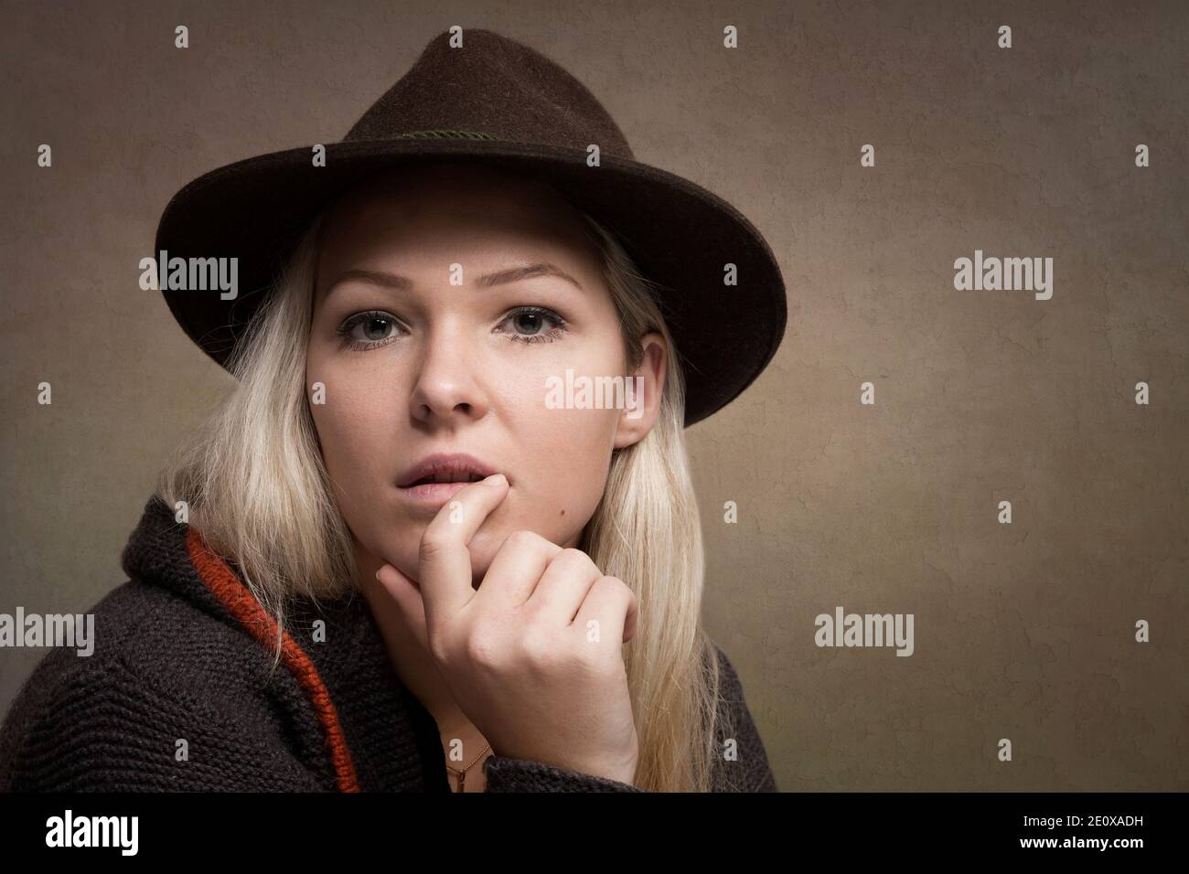 Portrait Shot Of A Young Woman With Blond Hair And A Brown Loden Hat Who Looks Thoughtfully At The Viewer Stock Photo