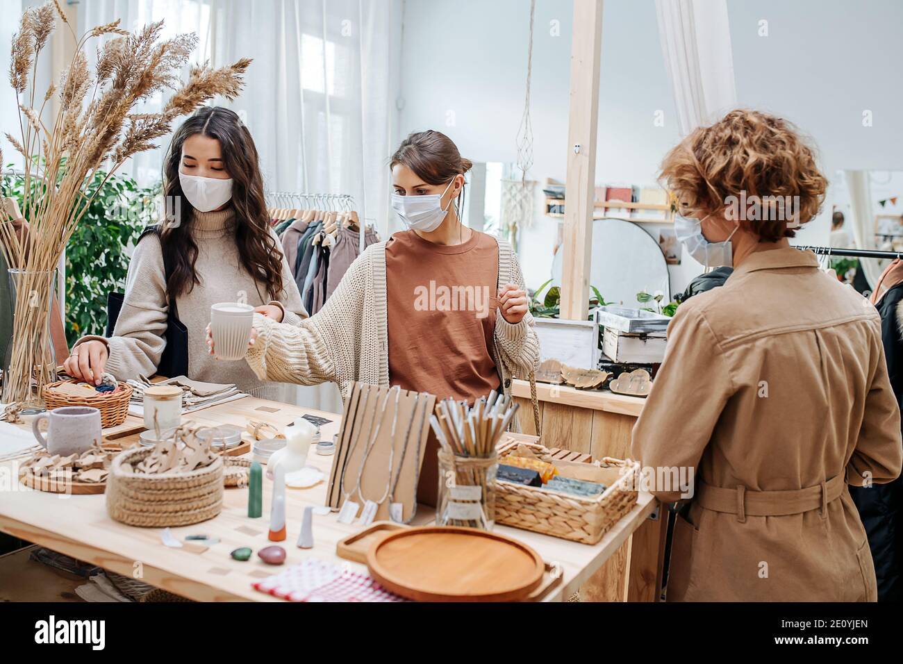 Three young women in ecological shop choosing between various cosmetic products Stock Photo