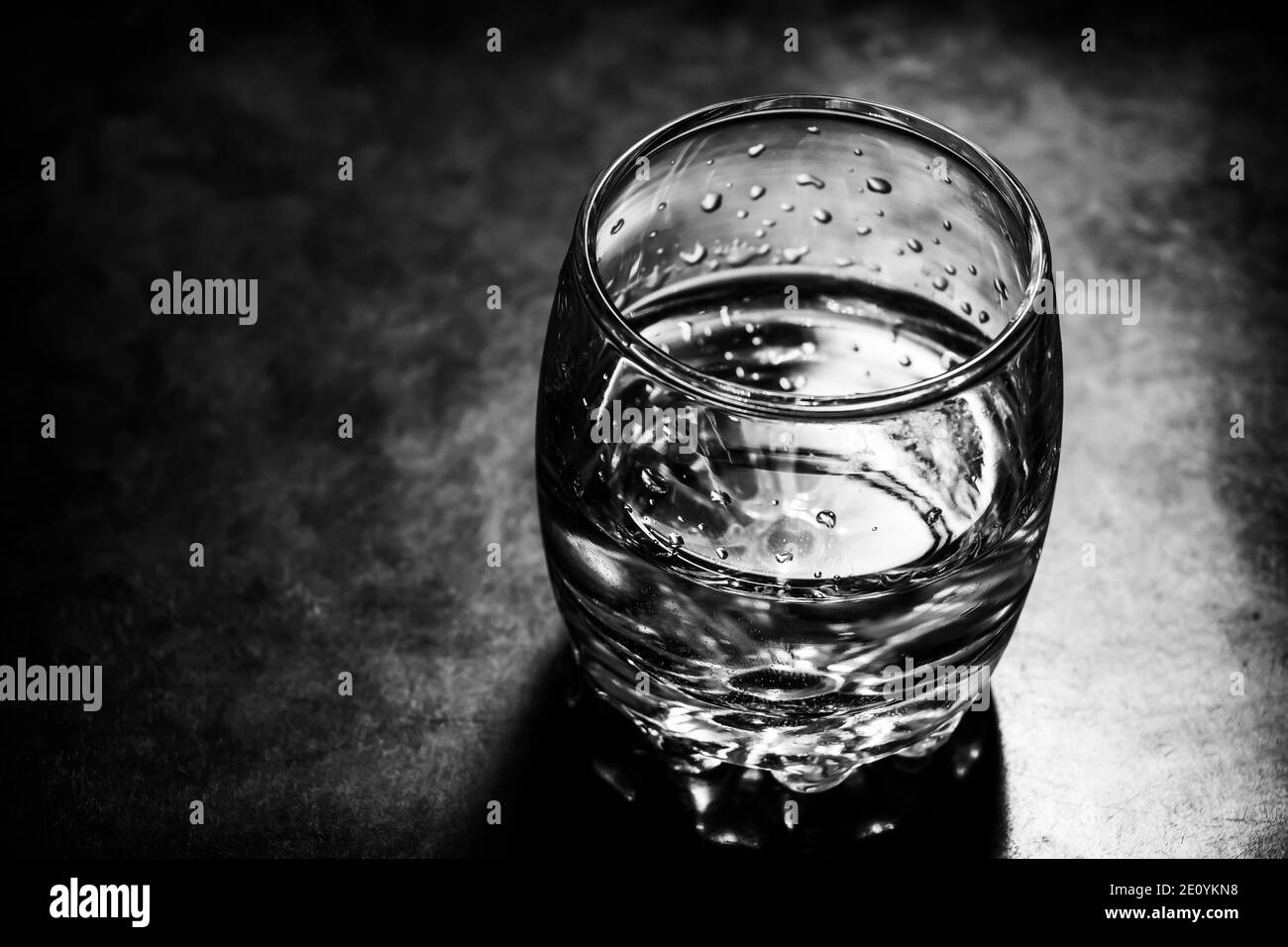 Glass of vodka is on the surface of the black table. Black and white photo. Stock Photo