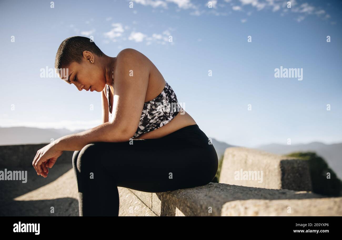 Side view of a woman relaxing outdoors after workout. Tired woman relaxing after outdoor training session. Stock Photo