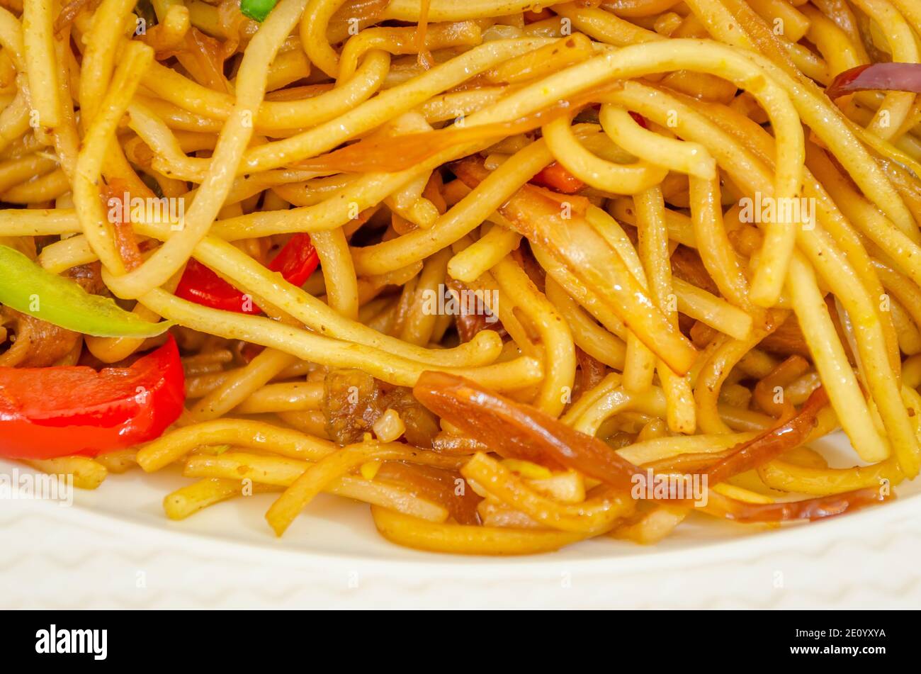 Closeup of Chicken Hakka Noodles in a white plate with added tomatoes and other vegetables Stock Photo