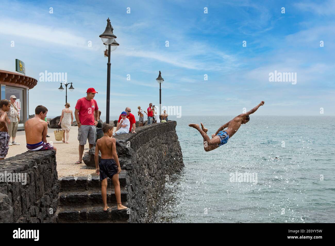 Boy jumps into the sea from the quay wall with Superman gesture Stock Photo