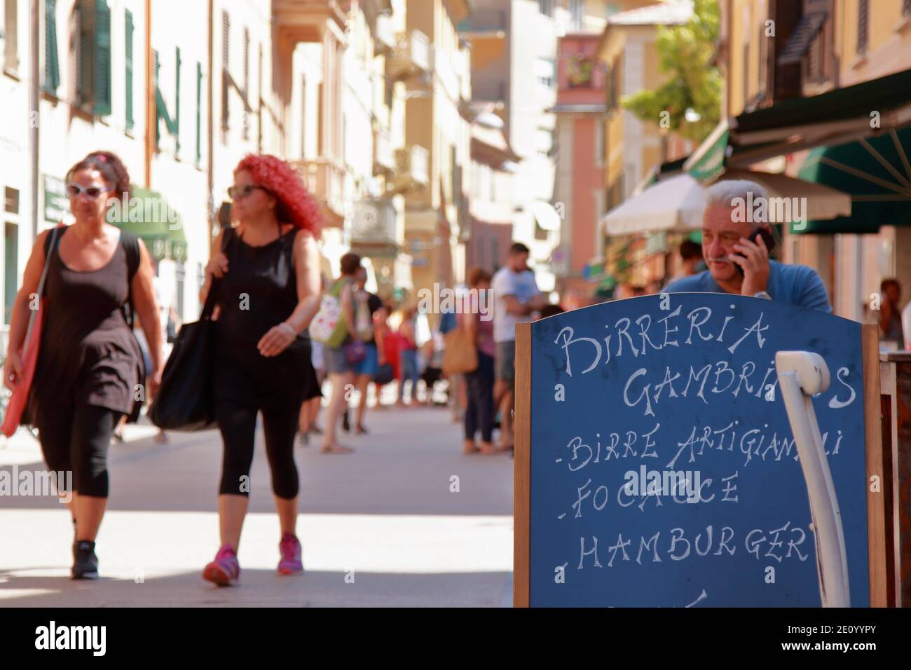 Lerici, Italy-summer2020: tourists stroll the central street and a man and sit behind the menu of a Ligurian focacciaria Stock Photo