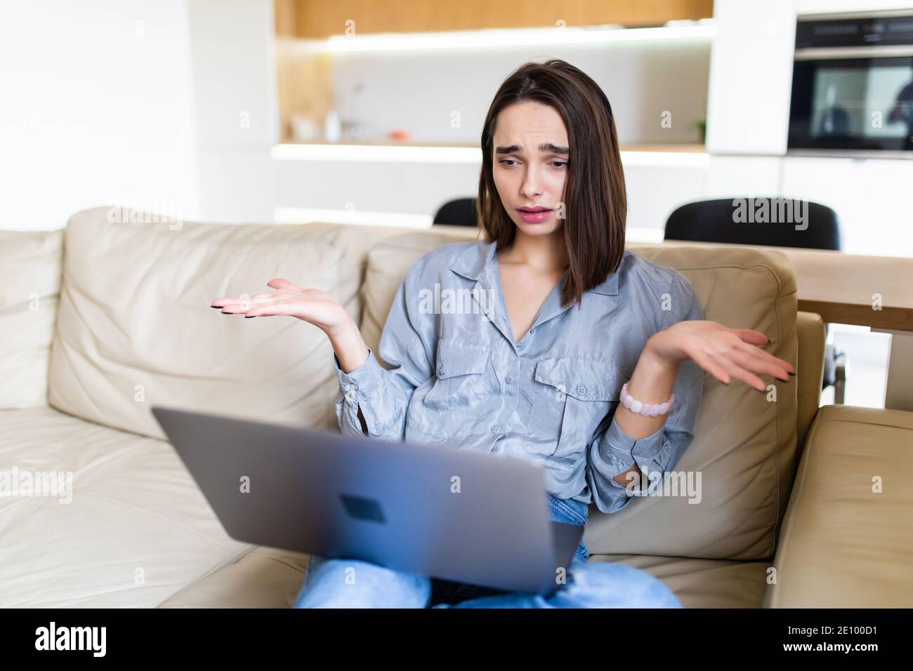 Angry young woman sit on couch in living room having laptop operating problems, annoyed by slow internet connection, confused girl working from home Stock Photo