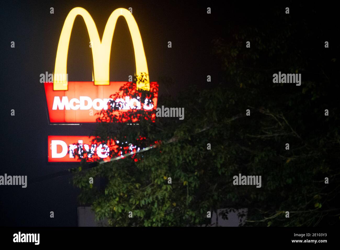 Lit Mcdonalds golden arches shot through trees against the night sky showing this famous fast food franchise in India Stock Photo