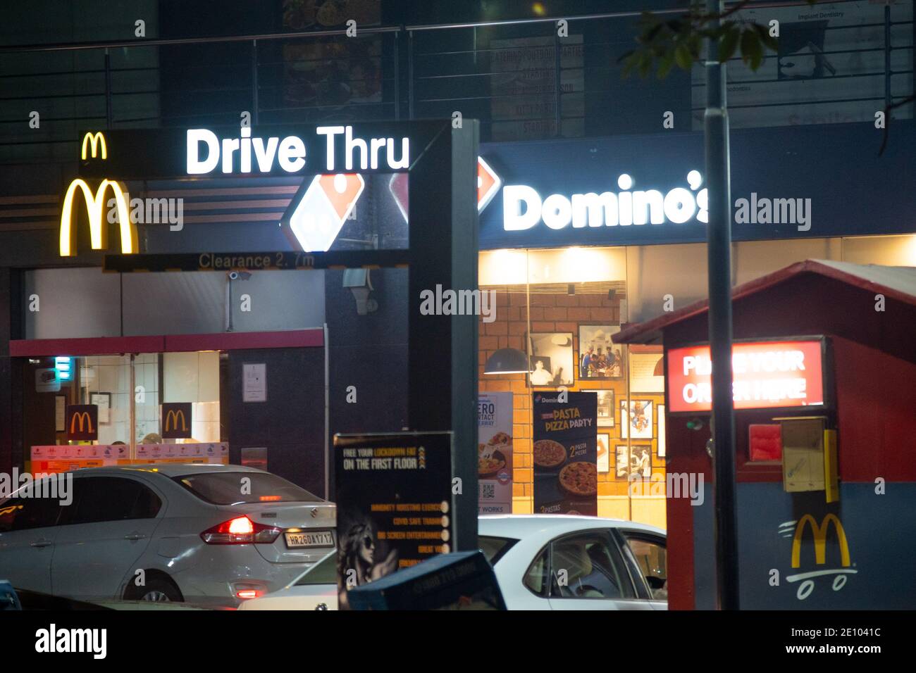 Lit signboard for a dominoes and Mcdonalds on a busy indian street with cars lining up for takeaway from the fast food quick service restaurant Stock Photo
