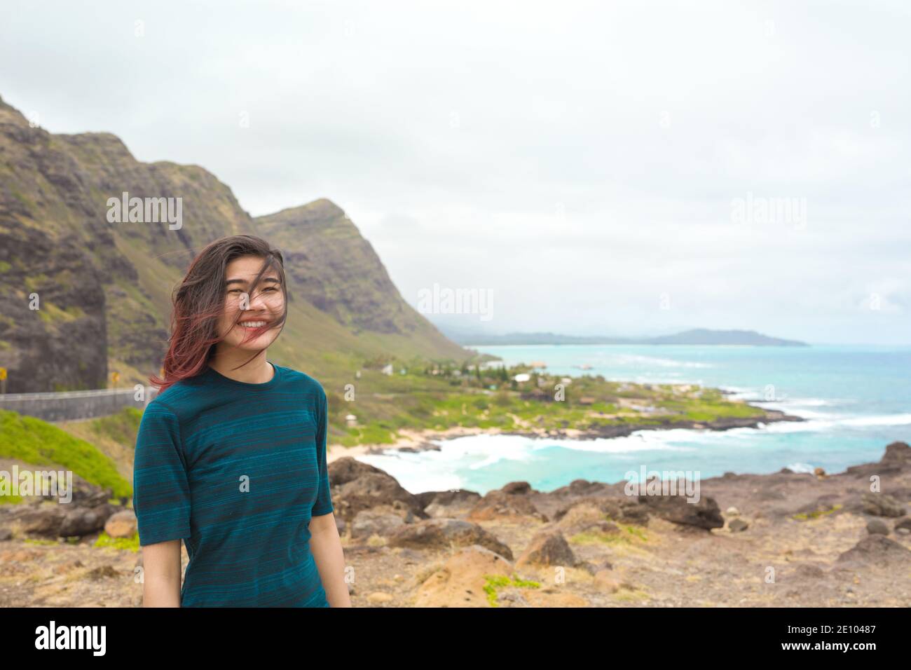 Biracial Asian Caucasian teen girl standing high above tropical hawaiian scenic view of blue ocean and green mountains on Oahu, Hawaii with Makapu'u B Stock Photo