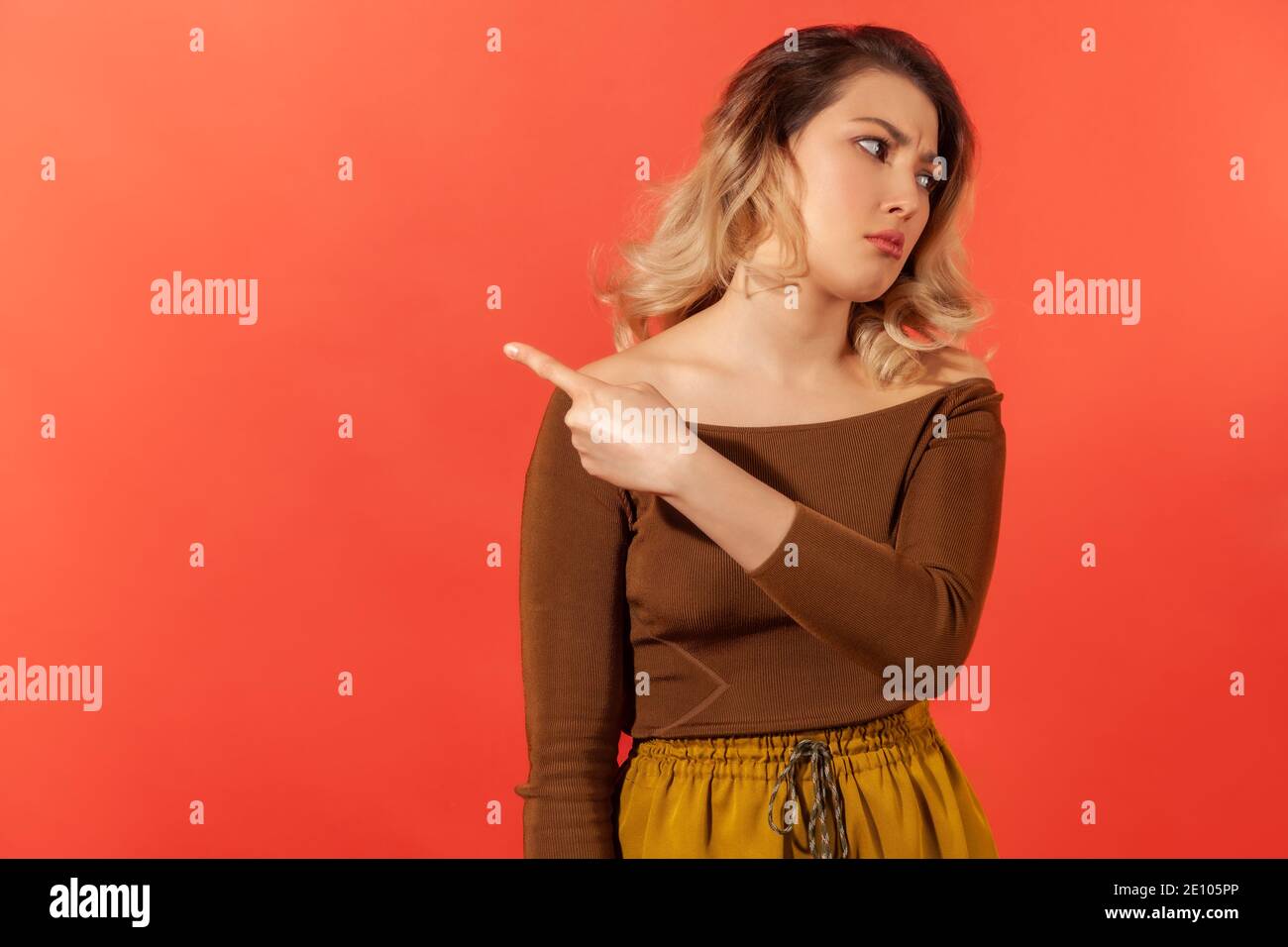 Get out! Irritated upset blonde woman in brown blouse pointing away, quarreling and scolding, showing exit with angry grimace, feeling betrayed. Indoo Stock Photo
